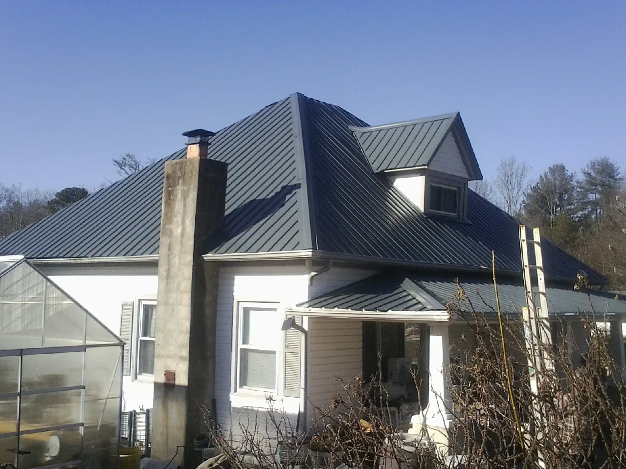 Dark blue standing seam metal roof on a white farmhouse with dormer — Slate & Tile Roof Repair by Roofing Brothers in Colgate