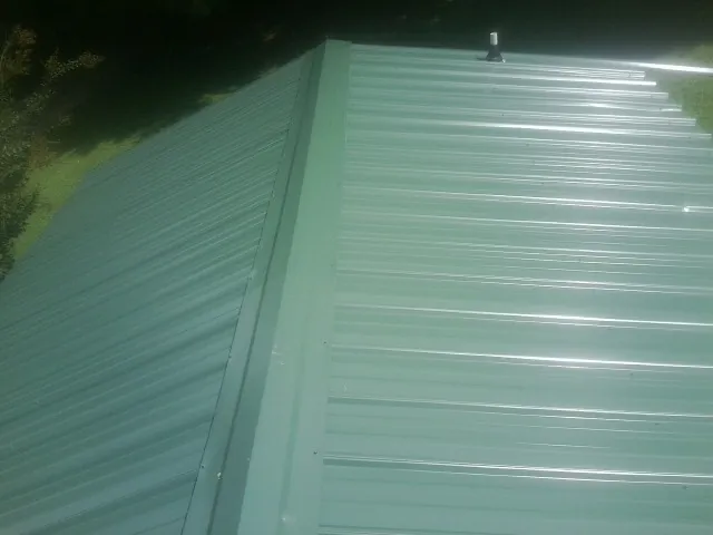 New green metal panels meeting at the ridge of a roof — Flat Roof Repair work by our crew in Colgate