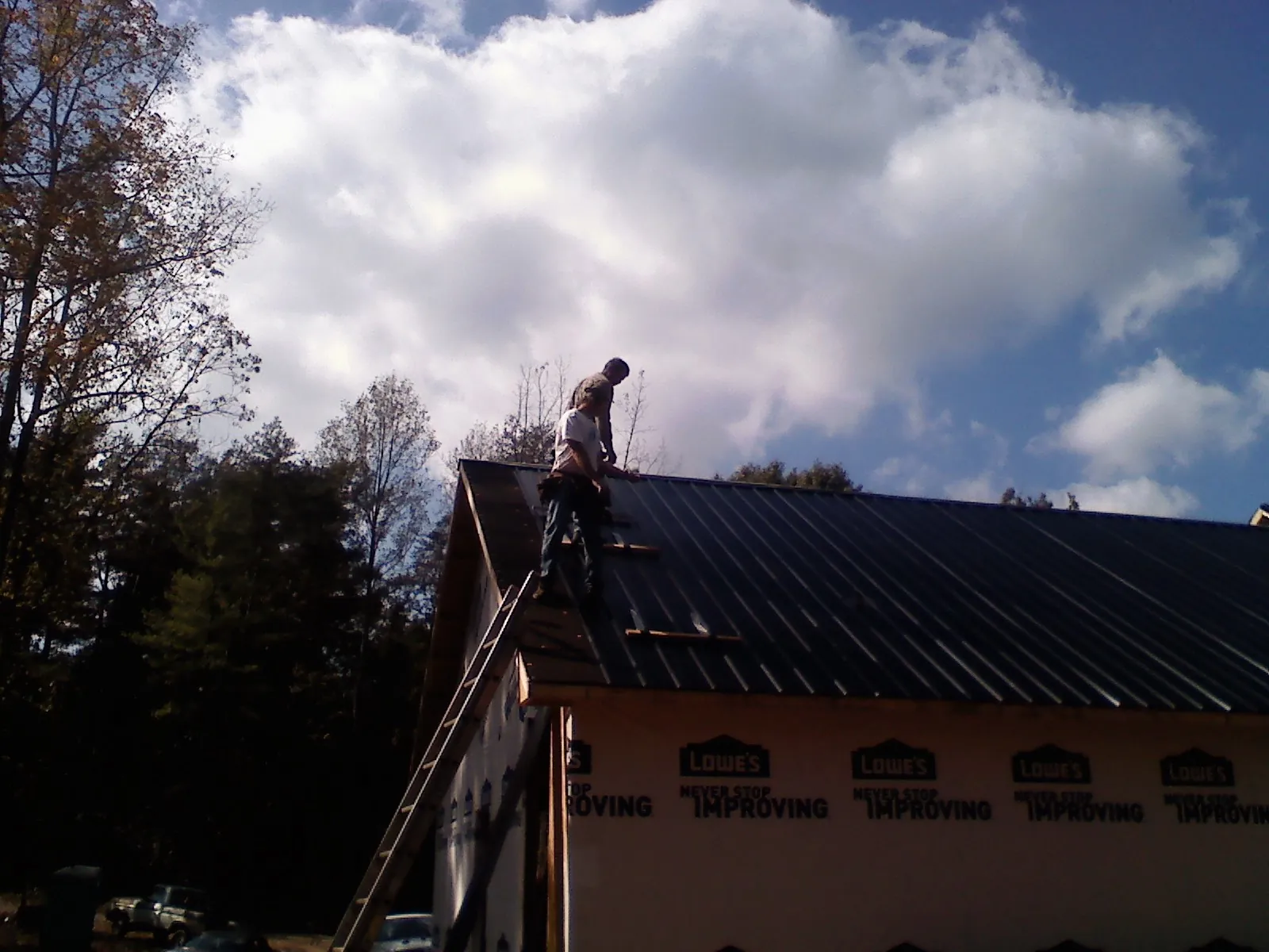 Roofer fastening dark metal panels high against a cloudy sky, from a Roof Inspection job in Colgate