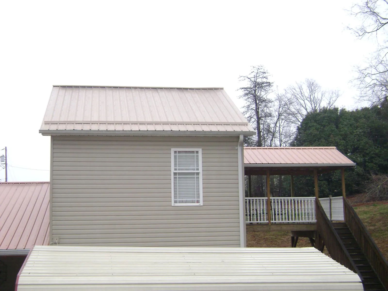 Tan metal roofs on a two story addition and attached porch, from a Roof Replacement job in Colgate